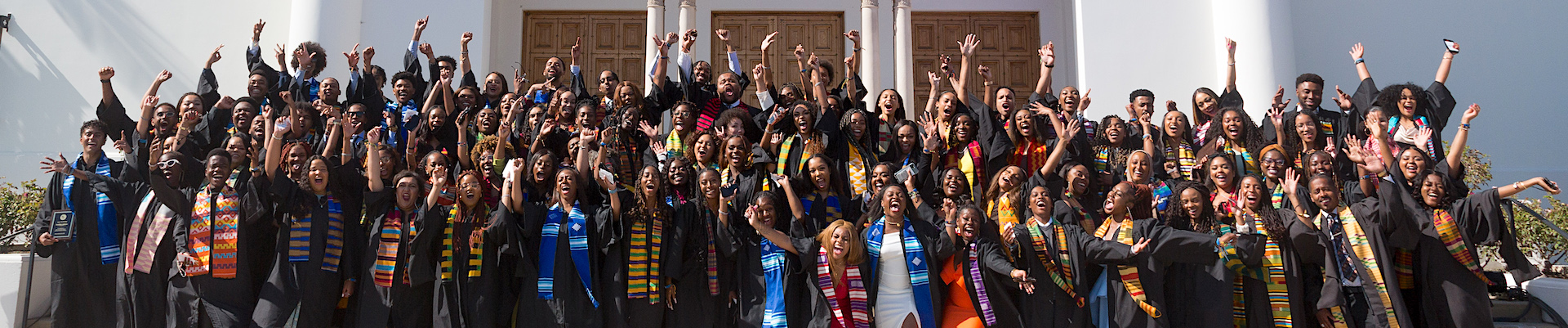 Kente graduates with hands raised in celebration